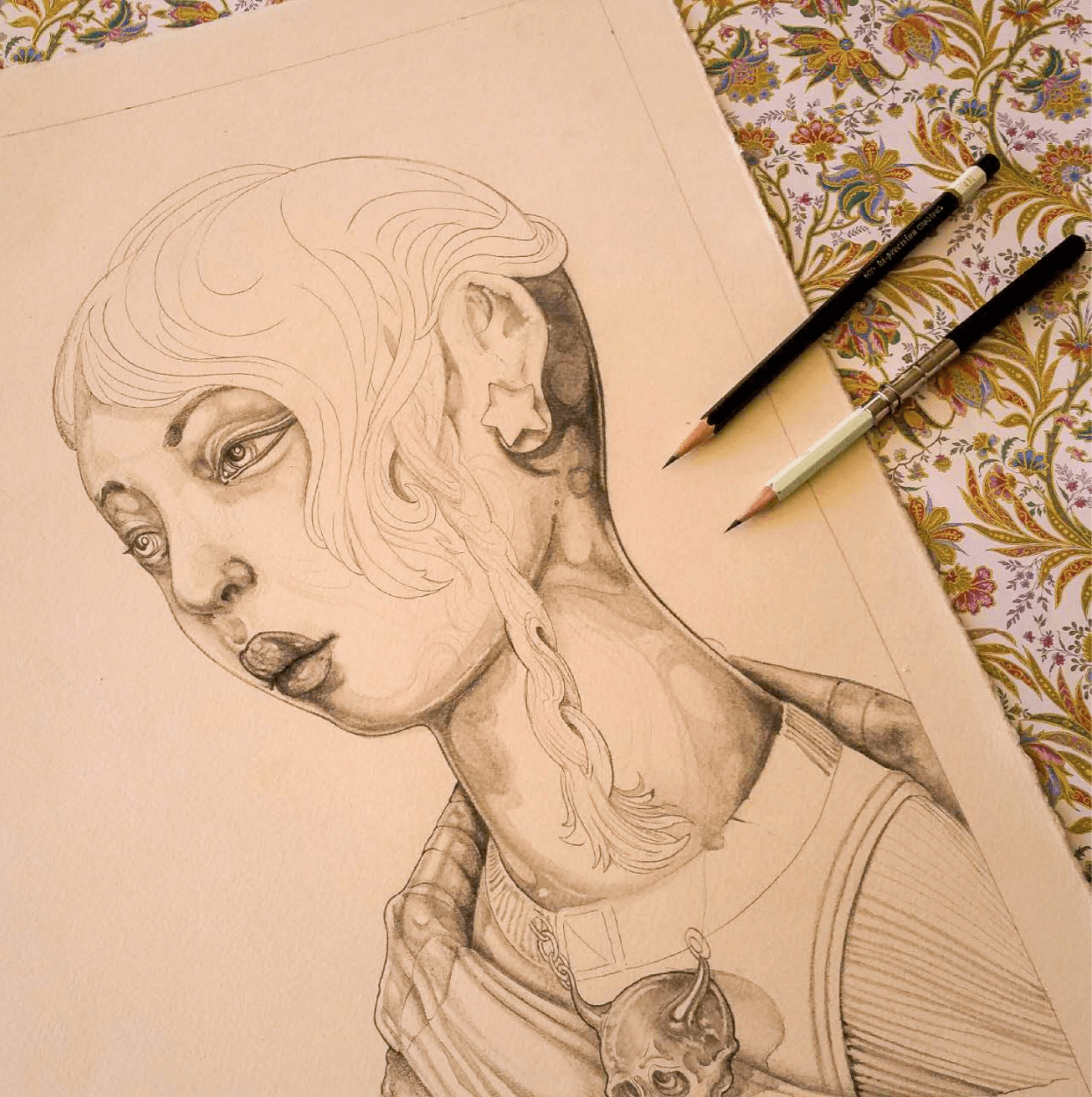 Sketch of Kali's portrait, pale and not fully colored, sitting on an ornate tablecloth with two pencils.