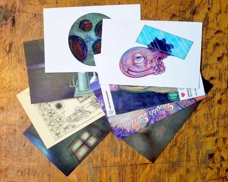 Many different postcards with strange and spooky artwork spread out on a wooden table.